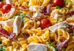 A bowl of Easy Chicken Club Pasta Salad garnished with fresh herbs and vegetables.