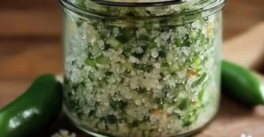 Homemade jalapeño salt in a glass jar with fresh jalapeños on the side.