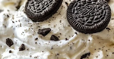A bowl of Protein Oreo Fluff Dessert topped with crushed Oreos and whipped cream.