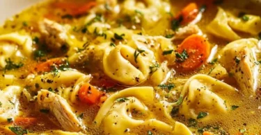 A warm bowl of cozy chicken tortellini soup garnished with herbs