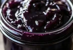 Jar of homemade blueberry butter with fresh blueberries on a wooden table.