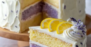 Lemon lavender cake with frosting and edible lavender flowers on a plate.