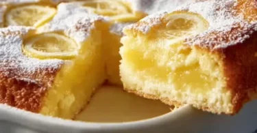 One-Bowl Lemon Cake topped with fresh lemon zest and icing on a white plate