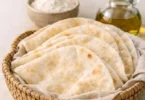 Soft and puffy Arabic bread (Kuboos) on a wooden table, showcasing its texture.