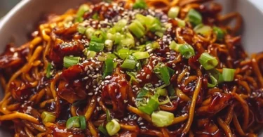 Delicious sticky garlic chicken noodles served in a bowl with green onions