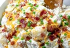 A bowl of loaded baked potato salad topped with cheese, bacon, and green onions