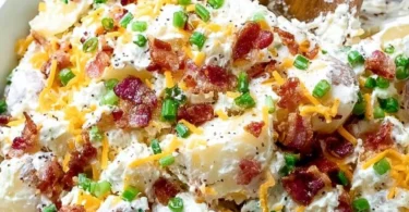 A bowl of loaded baked potato salad topped with cheese, bacon, and green onions