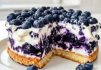 Slice of blueberry cake with vibrant blueberry cream frosting on a white plate