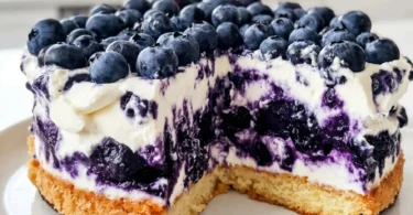 Slice of blueberry cake with vibrant blueberry cream frosting on a white plate