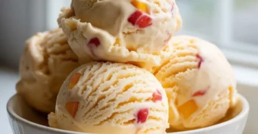 Bowl of homemade peach ice cream with fresh peaches and cream